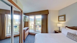 A hotel room with a bed, a desk, a chair, a window with curtains, a balcony, and a lamp. - Whistler - Cascade Lodge 633 (Whistler)
