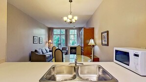 Ein Hotelzimmer mit Küchenzeile, einem Essbereich mit Tisch und Stühlen, einer Couch und einem großen Fenster mit Blick auf Grünflächen.