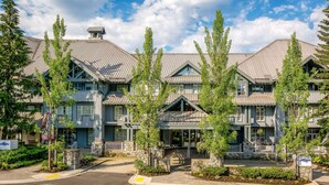 Ein mehrstöckiges Hotel im traditionellen Baustil, mit Fassaden aus Stein und Holz, zahlreichen Balkonen und einem zentralen Eingang mit Stufen.
