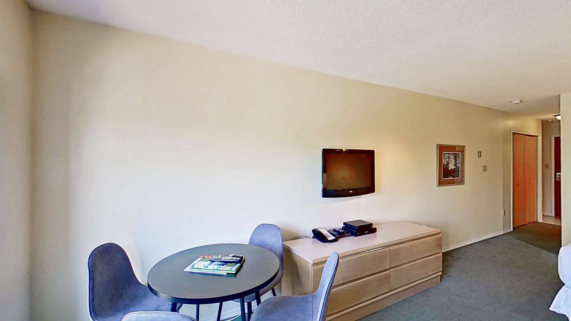 Una habitación de hotel con una mesa redonda, dos sillas, un televisor de pantalla plana montado en la pared, un teléfono y un aparador.