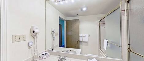 Une salle de bain d’hôtel avec un grand miroir, deux sèche-cheveux, un lavabo et un porte-serviettes.