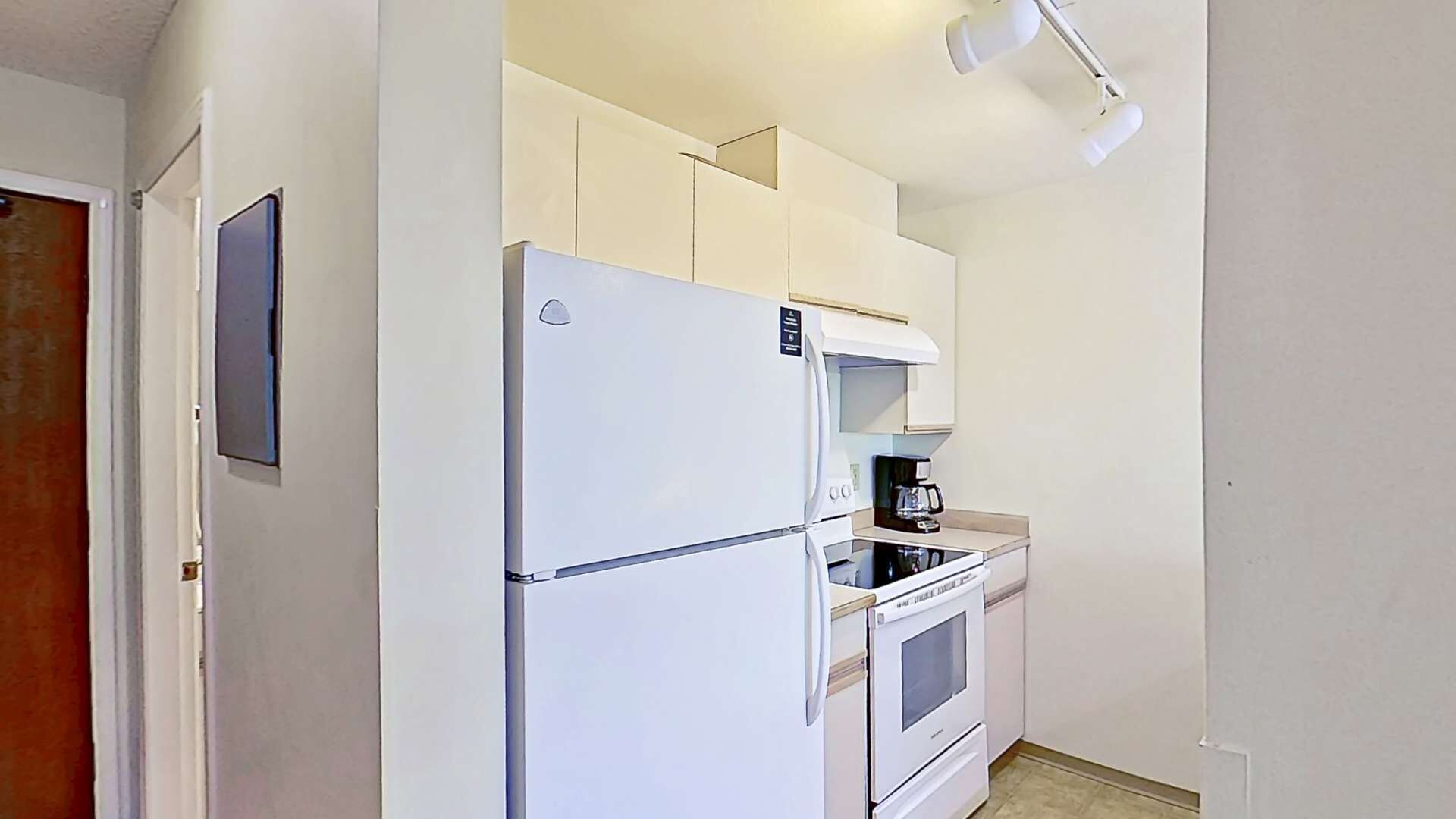 Eine kleine Küche mit Kühlschrank, Backofen und Kaffeemaschine.