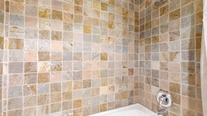 A bathroom with a tiled shower wall and a bathtub.
