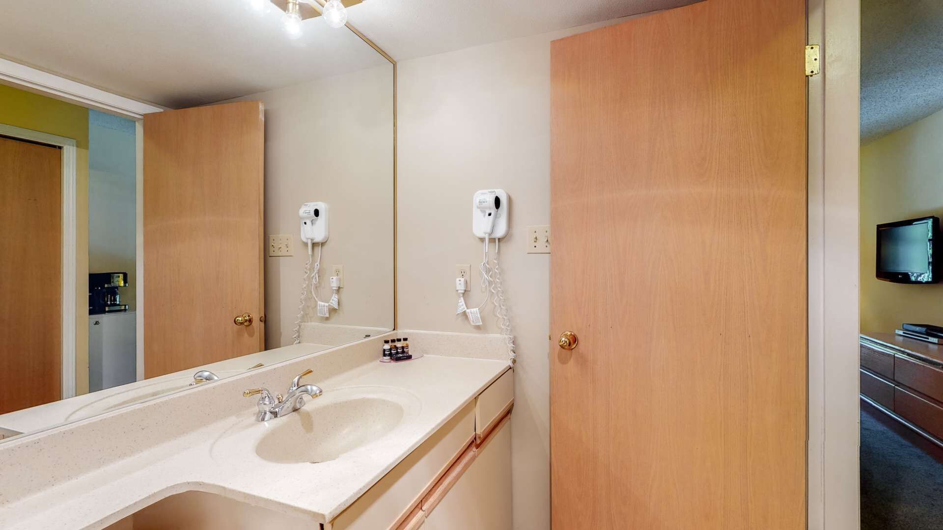 Een badkamer met een grote spiegel, een wastafel en twee haardroger op de muur bevestigd.