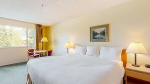 Une chambre d’hôtel avec un grand lit, deux lampes de chevet, un bureau avec une chaise et une fenêtre avec des rideaux.