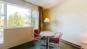 Une chambre d’hôtel avec une grande fenêtre, deux chaises, une petite table et une lampe.