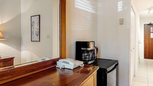 Habitación de hotel con una encimera de madera, cafetera, teléfono e impresión botánica enmarcada en la pared.