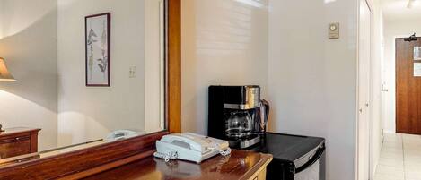 A hotel room with a wooden counter, a coffee maker, a telephone, and a framed botanical print on the wall.