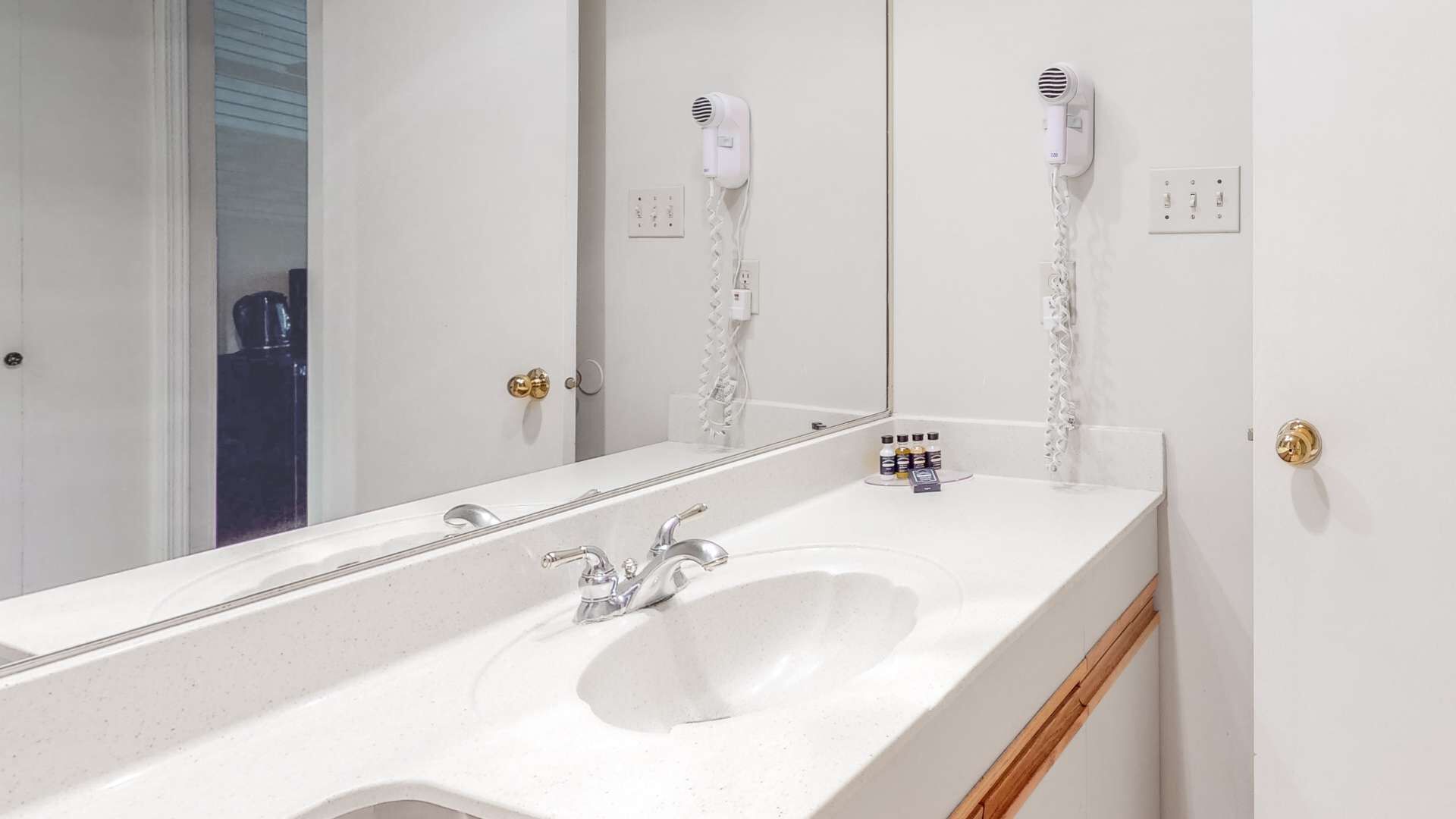 A bathroom with a white sink, a mirror, and two hair dryers mounted on the wall.