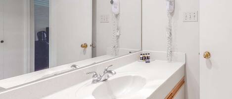 A bathroom with a white sink, a mirror, and two hair dryers mounted on the wall.