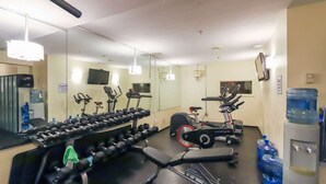 Un gimnasio con equipo de ejercicio, dispensador de agua y un espejo.