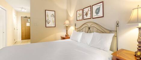 A hotel room with a large bed, a wooden nightstand with a lamp, and three framed botanical prints on the wall.