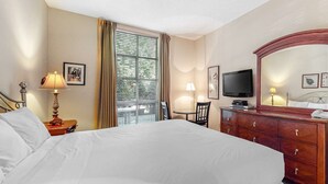 Una habitación de hotel con cama, televisor, cómoda, silla y ventana con cortinas.