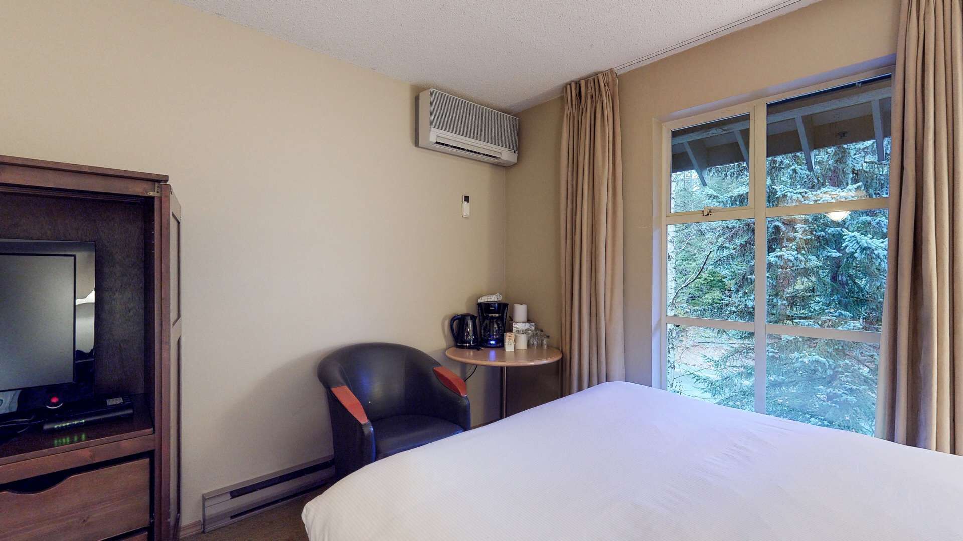 Een hotelkamer met een bed, een televisie, een koffiezetapparaat en een raam met gordijnen.