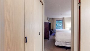 A hotel room with a wooden wardrobe, a bed, a window with curtains, and a small table. - Whistler - Glacier Lodge 232 (Whistler)