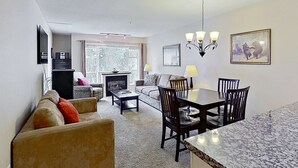 A living room with a sofa, a coffee table, a fireplace, and a dining area with a table and chairs. - Whistler - Glacier Lodge 252 (Whistler)