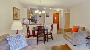 A living room with a sofa, a dining table with chairs, a kitchen area with a refrigerator and microwave, and a hallway leading to another room. - Whistler - Glacier Lodge 252 (Whistler)