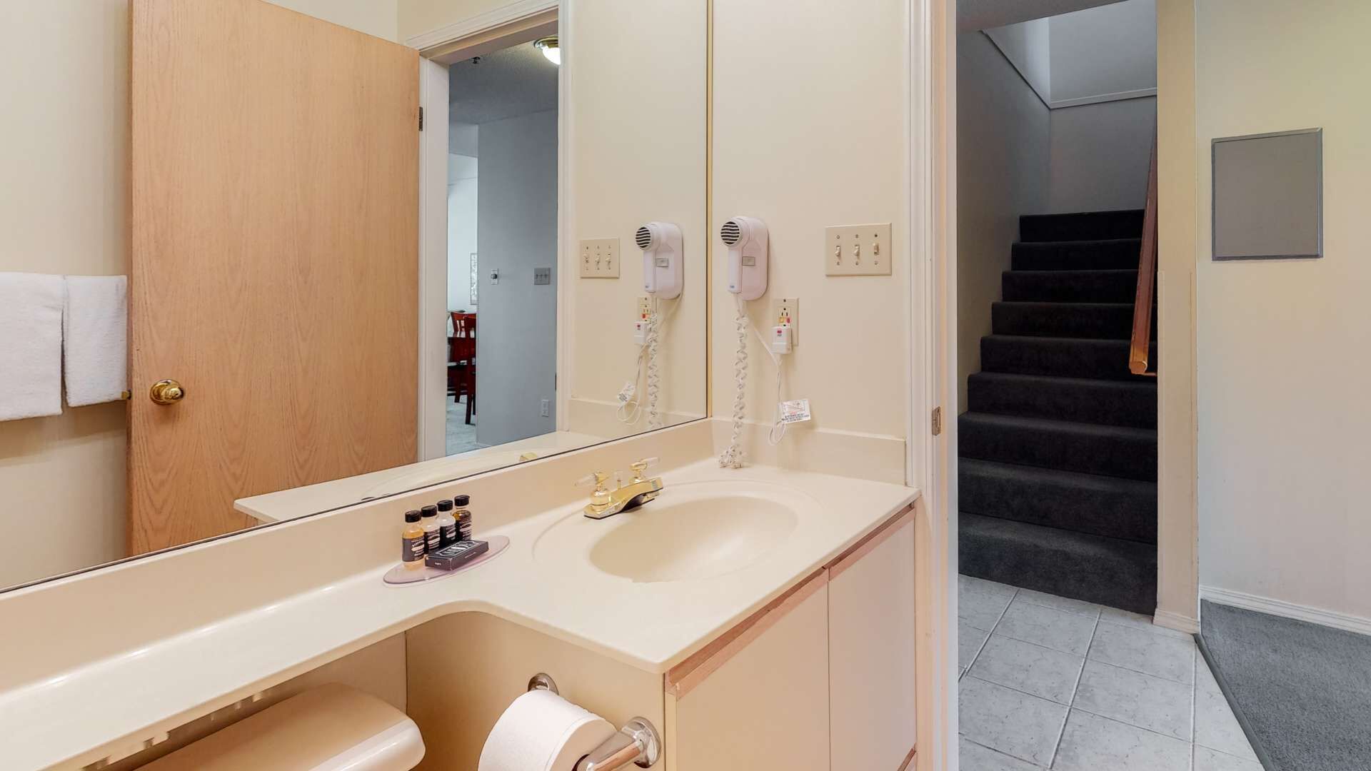 Een badkamer met een wastafel, spiegel en twee haardrogerhouders aan de muur.