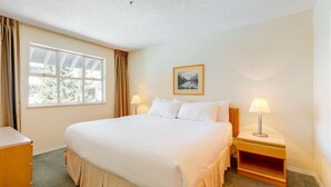 A hotel room with a large bed, two bedside lamps, a framed picture on the wall, and a window with curtains. - Whistler - Glacier Lodge 303 (Whistler)