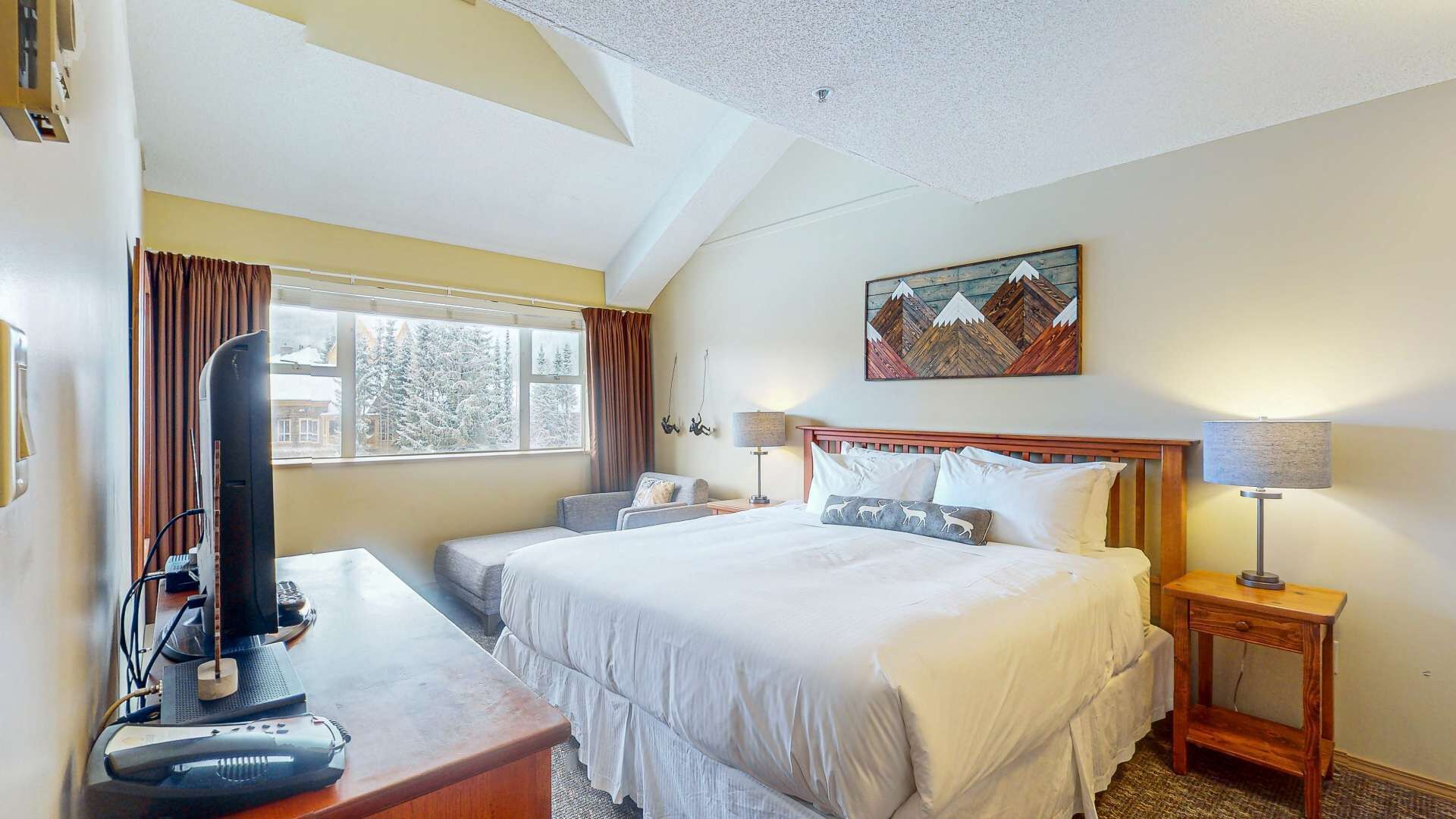 A hotel room with a bed, bedside tables, a desk with a computer, and a window with curtains.