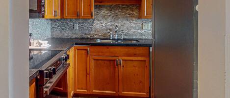 A kitchen with wooden cabinets, a black countertop, a tiled backsplash, and a stainless steel sink.