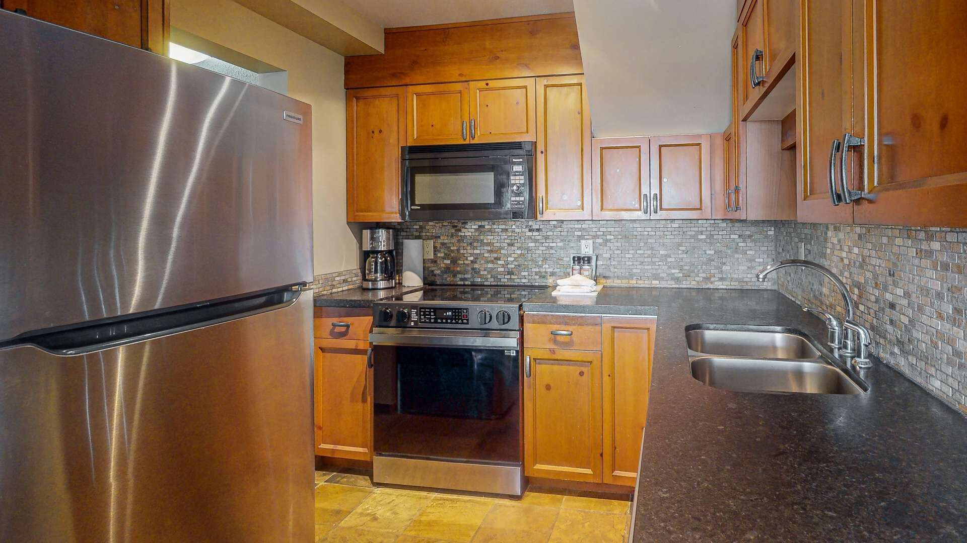 Una cocina con armarios de madera, un refrigerador de acero inoxidable, un microondas, un horno, una cafetera y un lavamanos.