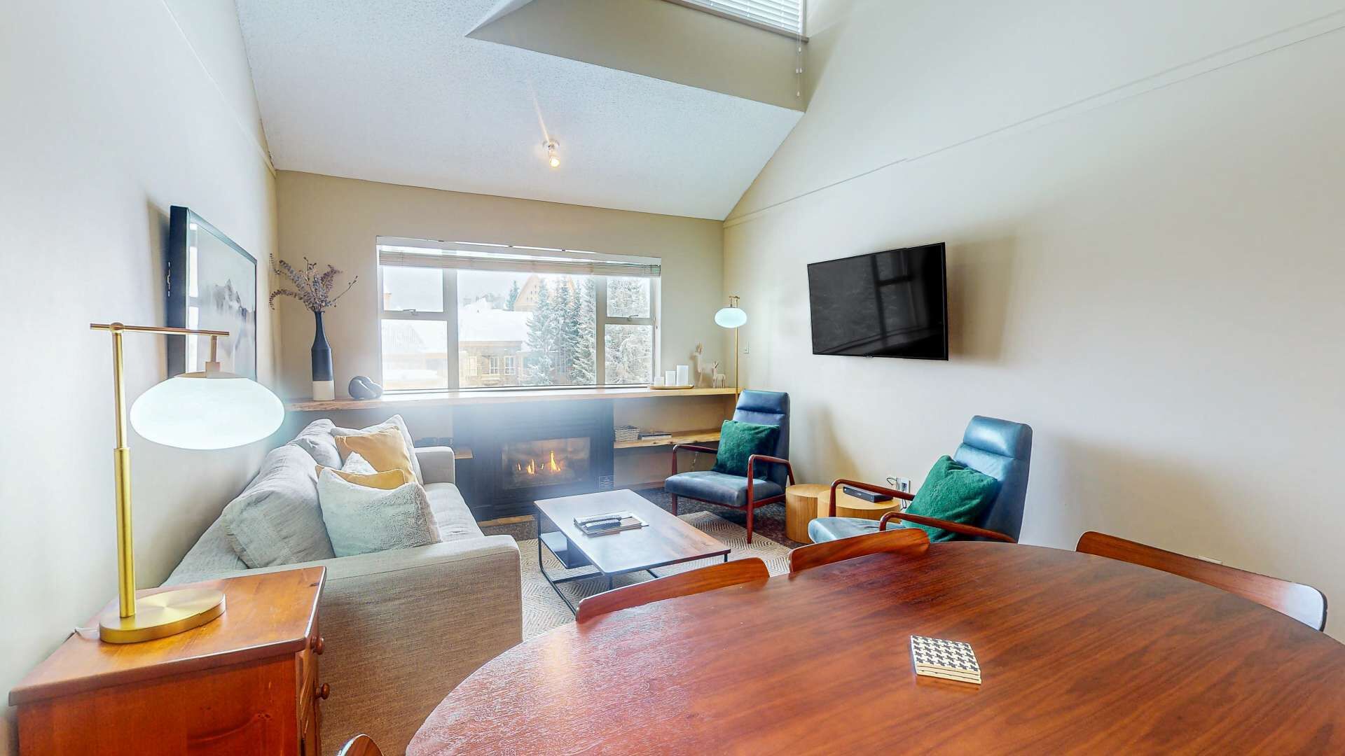 Una sala de estar moderna con chimenea, una mesa de comedor redonda de madera, un sofá y dos sillones.