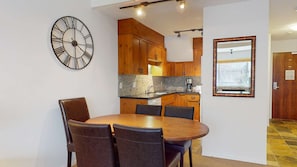 A modern kitchen with wooden cabinets, a round dining table with chairs, and a large wall clock.