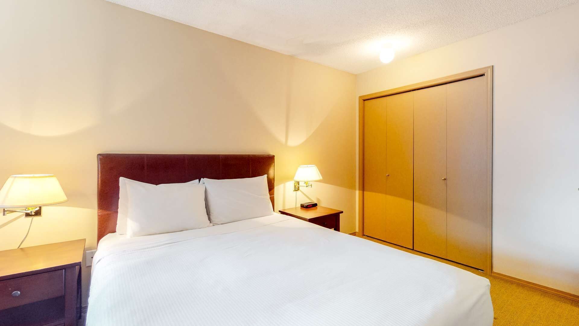 Ein Hotelzimmer mit einem Bett, zwei Nachttischlampen, einem Nachttisch und einem Kleiderschrank.