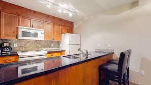 A kitchen with wooden cabinets, a microwave, a stove, a refrigerator, a sink, and a bar stool. - Whistler - Glacier Lodge 341 (Whistler)