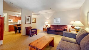 A modern living room with a sofa, armchair, and coffee table. There is a kitchen area with cabinets and a microwave visible. - Whistler - Glacier Lodge 341 (Whistler)