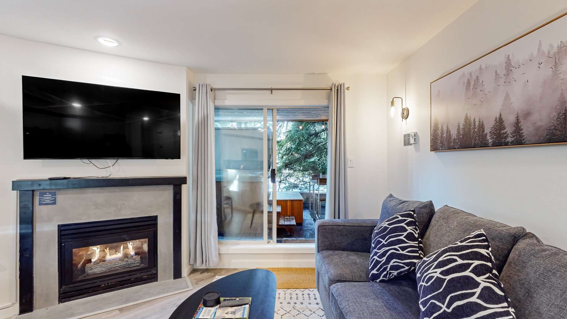 A modern living room with a fireplace, a flat-screen TV, a sofa with patterned cushions, and a painting on the wall.