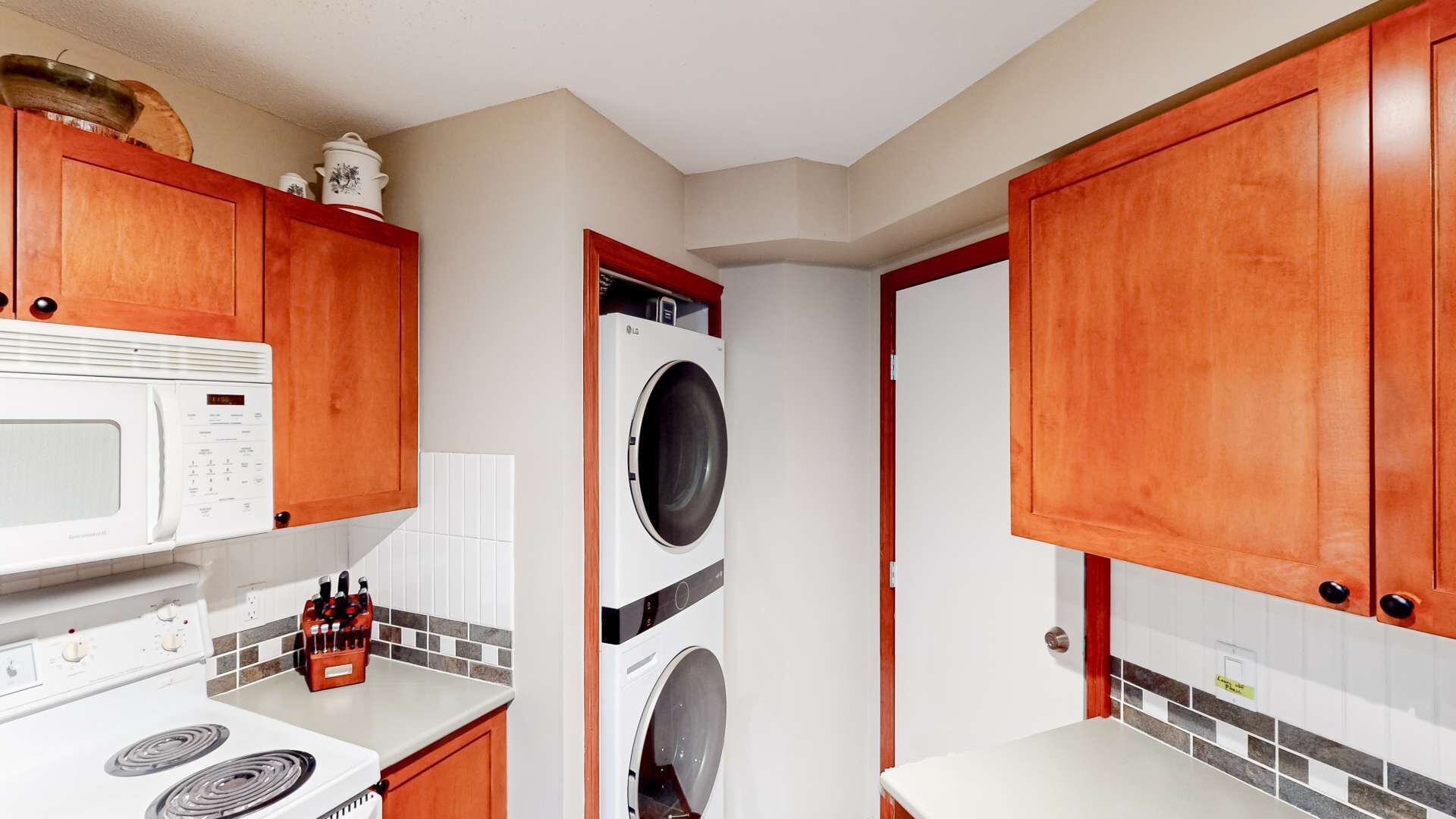 Una cocina con armarios de madera, microondas, estufa y lavadora.