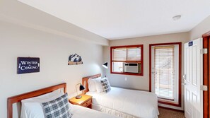 A room with two beds, a nightstand, a lamp, a window with blinds, a door with a number, and a wall decoration. - Whistler - Glacier's Reach 42 (Whistler)