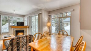 A cozy dining area with a fireplace, stone walls, and large windows offering a view of a snowy landscape.