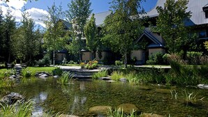 A landscaped garden with a pond, trees, and a building with a blue roof.