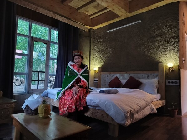 A room with a bed, a window, a table with a plant, and a wall-mounted light fixture. - Aama Homestay (Spiti)
