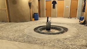 Ein Innenhof mit einem zentralen Feuerkorb, umgeben von einem Kiesweg. Holzdecken und ein hängender Kleiderhaken sind ebenfalls zu sehen.