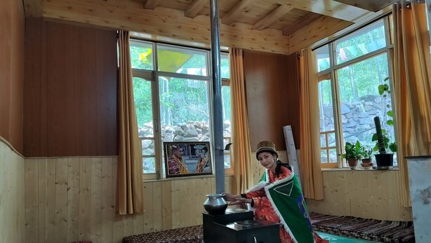 Een kamer met houten wanden en een groot raam, een fornuis en een bed met beddengoed met een patroon.