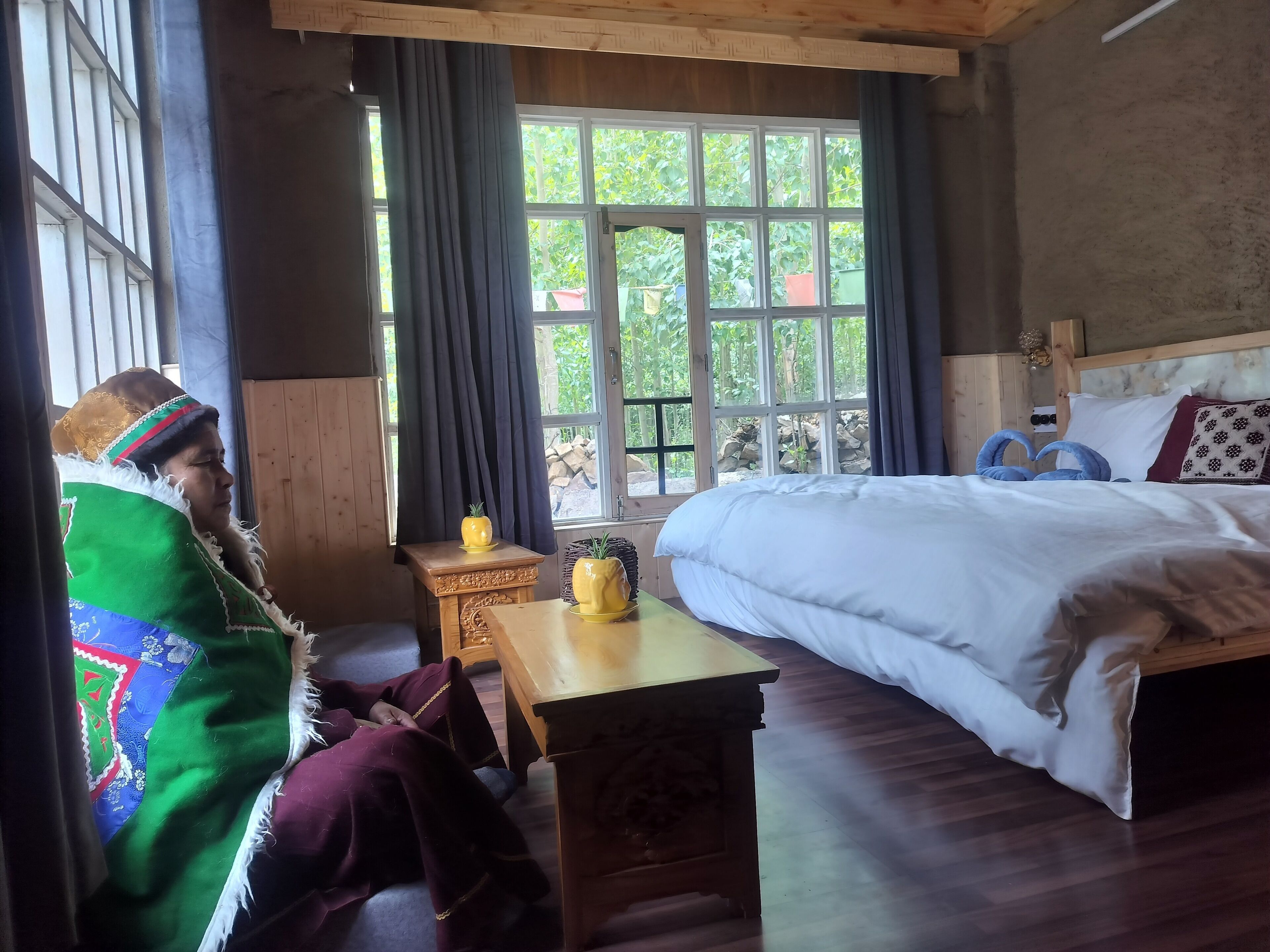 A room with a bed, a wooden nightstand, a small table, and a window with curtains.