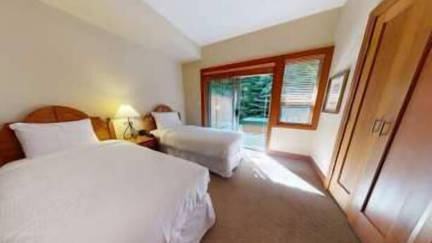 A hotel room with two beds, a nightstand, a lamp, and a view of the outdoors through a window. - Whistler - Montebello #33 (Whistler)