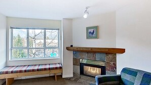 A cozy room with a large window, a bench, a fireplace, and a framed picture on the wall. - Whistler - Marketplace Lodge 338 (Whistler)