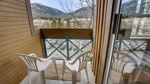 A balcony with a wooden floor, a glass door, and a view of a parking lot and mountains. - Whistler - Marketplace Lodge 338 (Whistler)