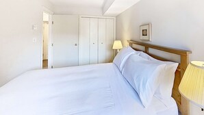 A bedroom with a large bed, a wooden headboard, a bedside lamp, a door, and a framed picture on the wall. - Whistler - Marketplace Lodge 338 (Whistler)