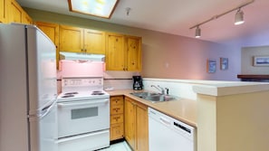 A kitchen with wooden cabinets, a white refrigerator, a stove, a dishwasher, and a sink. - Whistler - Marketplace Lodge 220 (Whistler)