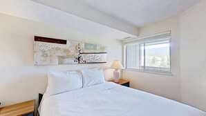 A bedroom with a bed, a nightstand with a lamp, a window with a view, and a wall art piece. - Whistler - Marketplace Lodge 348 (Whistler)