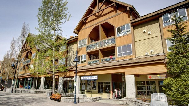 A multi-story wooden building with balconies, storefronts, and a bench in front. - Whistler - Marketplace Lodge 348 (Whistler)