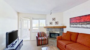A living room with a TV, a striped armchair, an orange sofa, a fireplace, and a large painting. - Whistler - Marketplace Lodge 348 (Whistler)