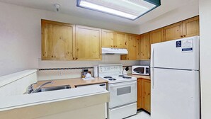 A compact kitchen with wooden cabinets, a white stove, a microwave, and a refrigerator. - Whistler - Marketplace Lodge 348 (Whistler)