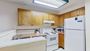 A compact kitchen with wooden cabinets, a white stove, a microwave, and a refrigerator. - Whistler - Marketplace Lodge 348 (Whistler)